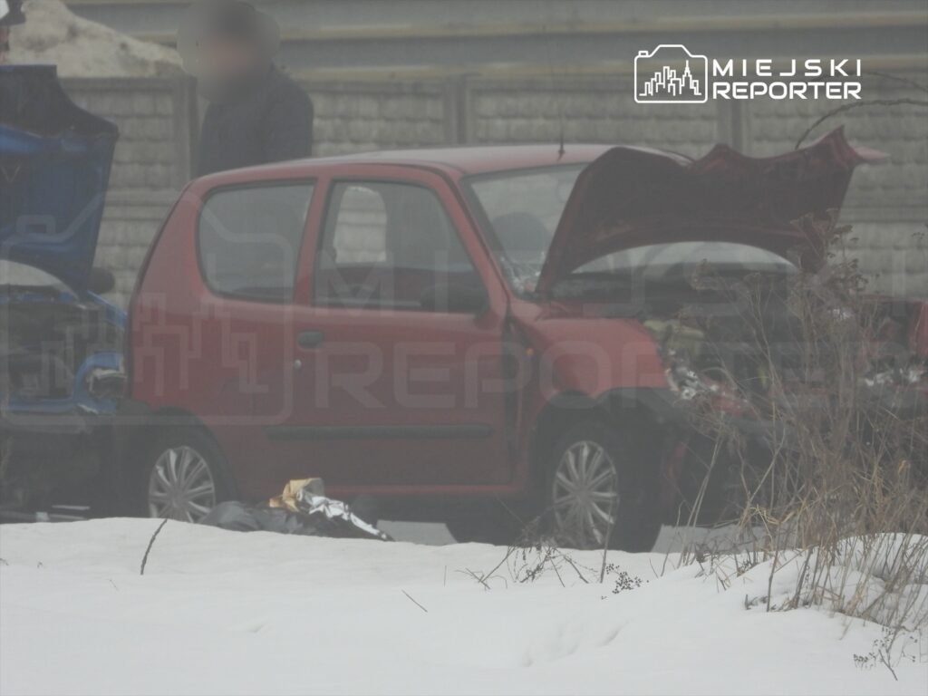 Czerwony samochód osobowy z otwartą maską stoi na zaśnieżonej drodze obok uszkodzonego niebieskiego pojazdu.