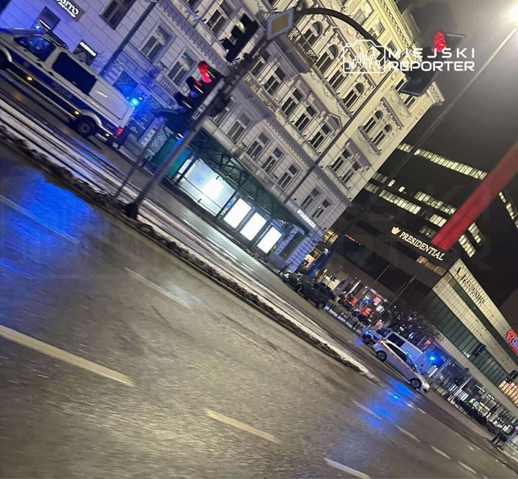 Policyjny radiowóz zaparkowany przy ulicy z widocznym sygnalizatorem świetlnym i oświetleniem nocnym.