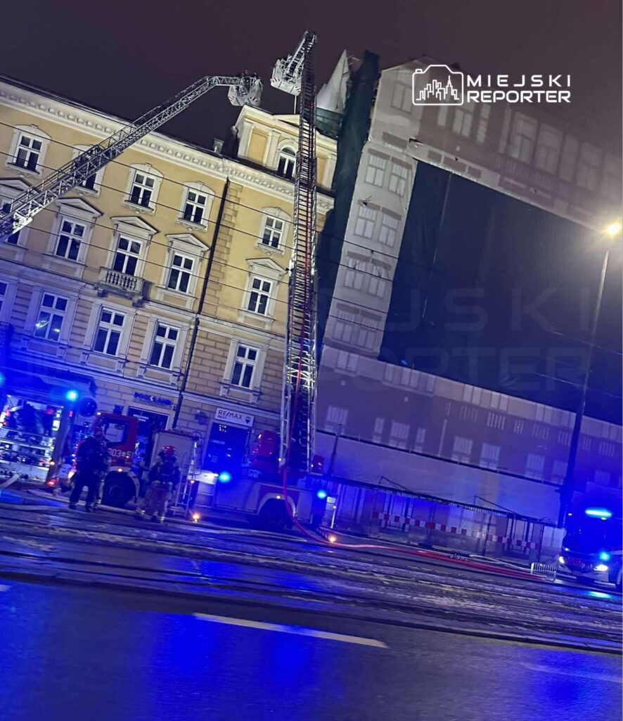 Strażacy w hełmach pracują przy wozach strażackich, używając drabin do akcji ratunkowej na oświetlonej ulicy.