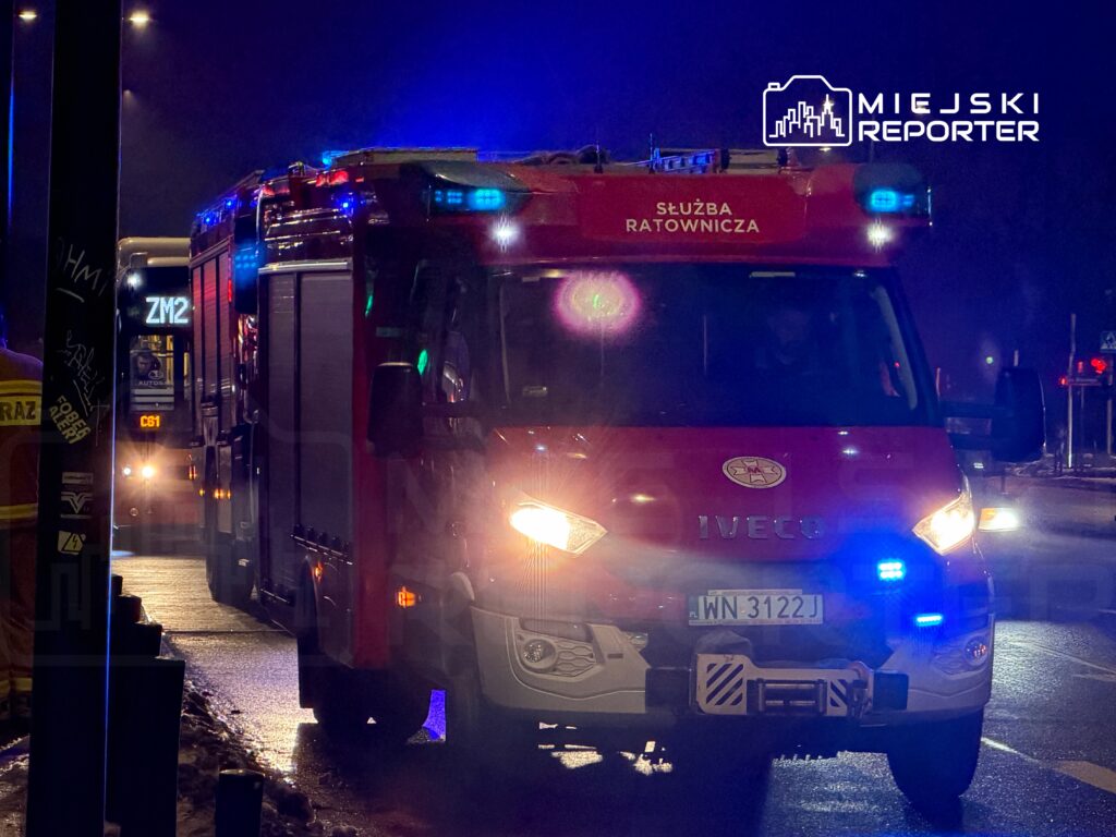 Czerwony wóz strażacki z włączonymi sygnalizacjami świetlnymi zatrzymany na ulicy w nocy.