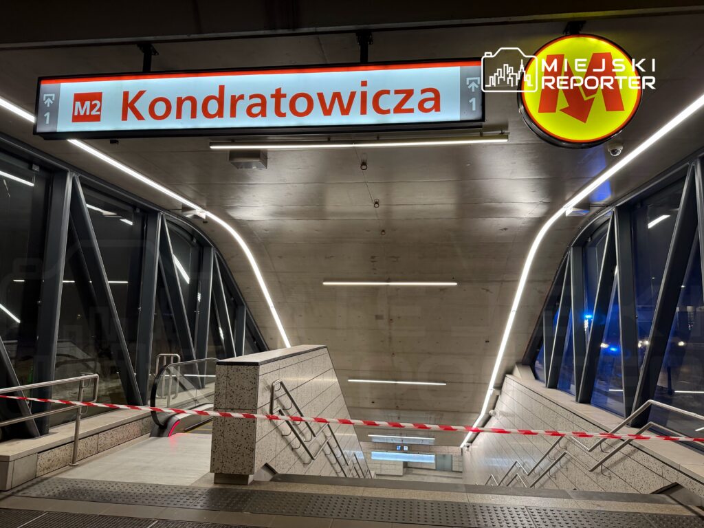 Stacja metra z oznaczeniem "Kondratowicza" i oświetleniem LED, schody zabezpieczone taśmą ostrzegawczą.