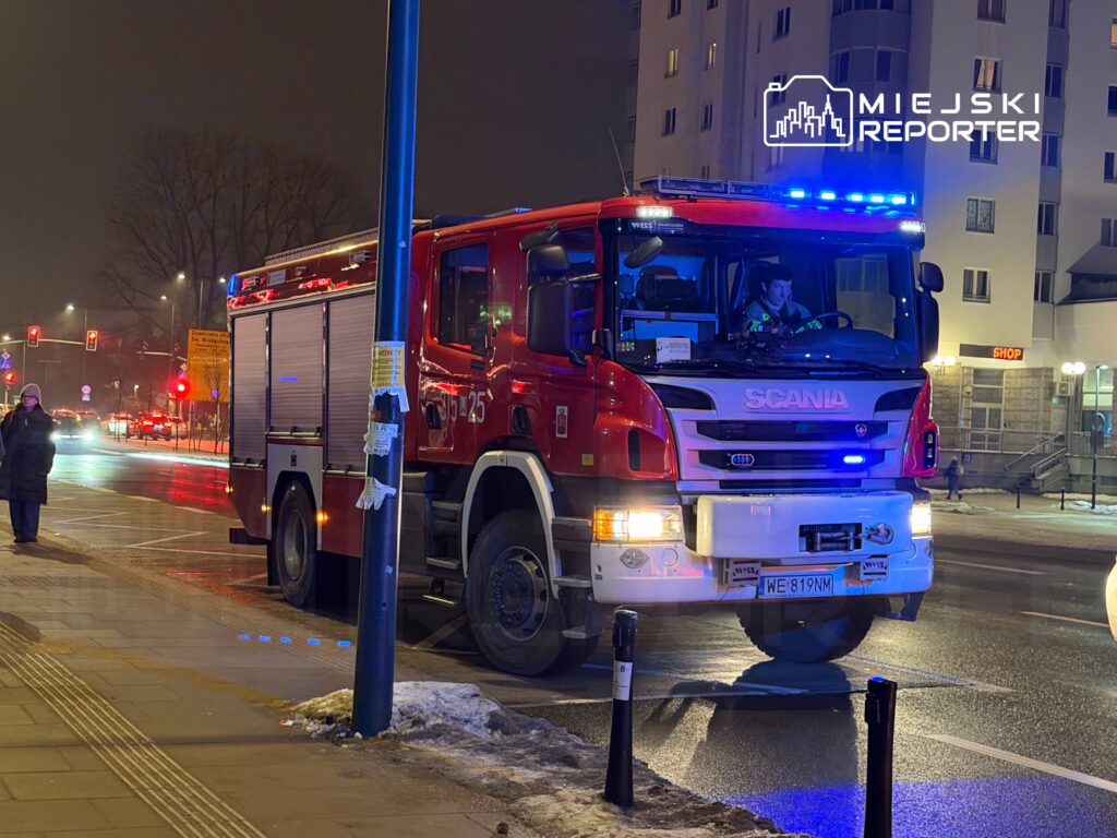 Czerwony wóz strażacki z włączonymi sygnalizatorami zatrzymany na oświetlonej ulicy w nocy.