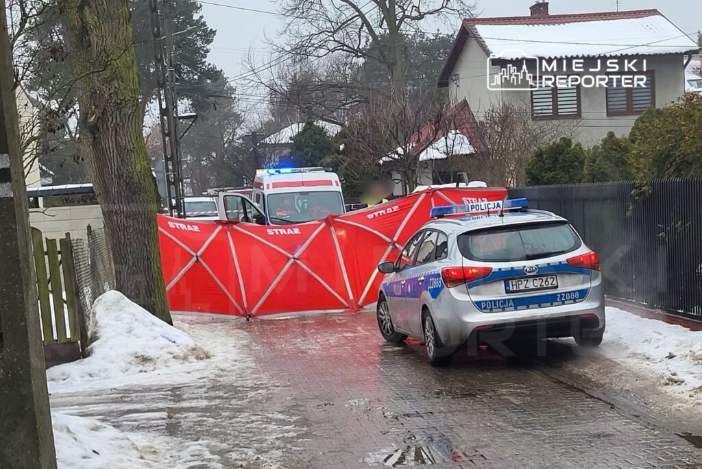 Na drodze stoi czerwony parawan zabezpieczający, obok zaparkowany radiowóz policji oraz samochód straży pożarnej.