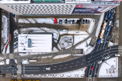 Widok z lotu ptaka na skrzyżowanie ulic z parkingiem, otoczone budynkami, pokryte śniegiem.