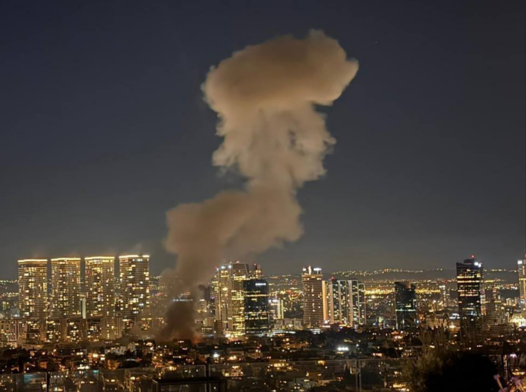 W nocy z miasta unosi się gęsty, szary dym, w tle widoczne oświetlone wieżowce.