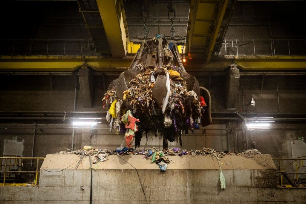 Hala recyklingowa z dźwigiem podnoszącym ładunek z odpadami, w tym kolorowymi foliami i tekstyliami.