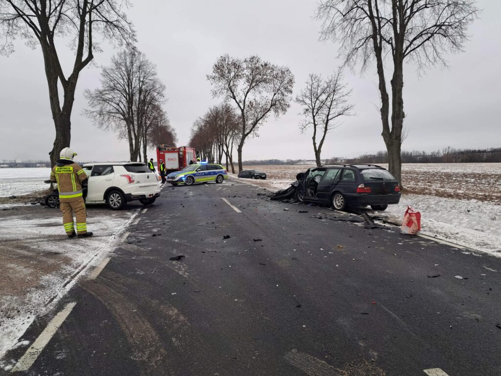 Na drodze w zimowym otoczeniu doszło do wypadku samochodowego; strażacy i policja udzielają pomocy.
