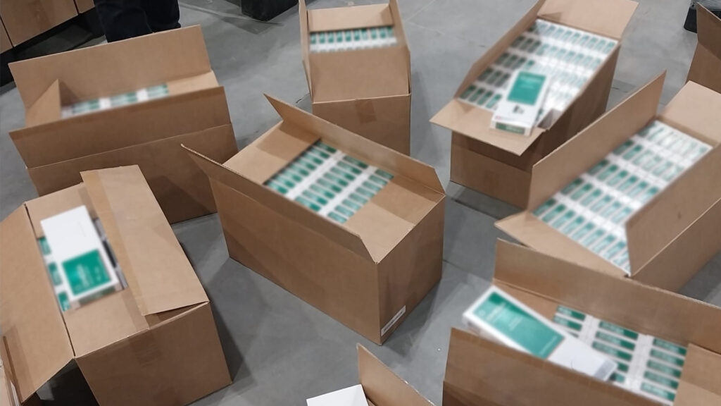 Kartony z papierosami ułożone na podłodze w magazynie, z widocznymi etykietami na opakowaniach.