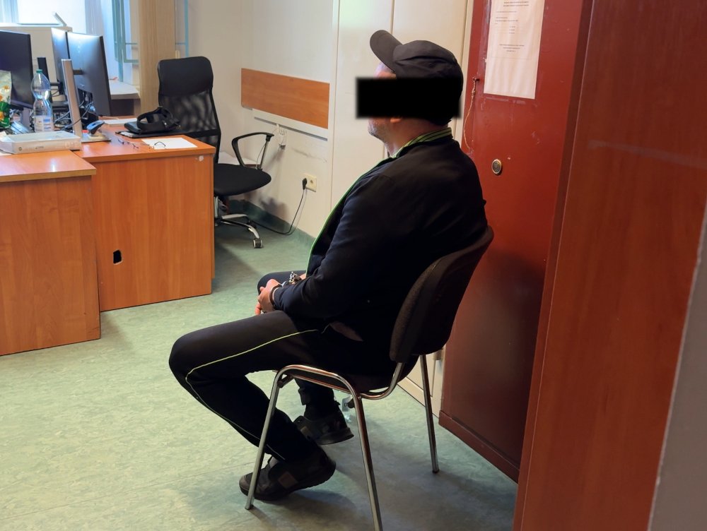 Mężczyzna w czapce siedzi na krześle w biurze, obok niego znajdują się biurka z komputerami.