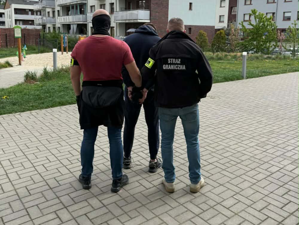 Funkcjonariusze Straży Granicznej zatrzymują mężczyznę na chodniku w osiedlu mieszkaniowym.