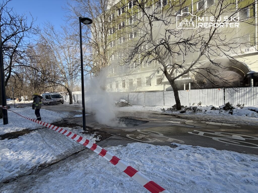 Strażak obserwujący wydobywający się z ziemi gorący parę w pobliżu zasłoniętej taśmą strefy na ośnieżonej ulicy.