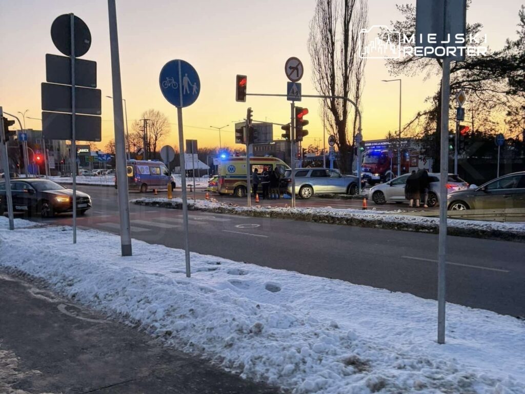 Na skrzyżowaniu ulic stoi karetka pogotowia oraz radiowóz, w tle widać pojazdy zatrzymane na czerwonym świetle.