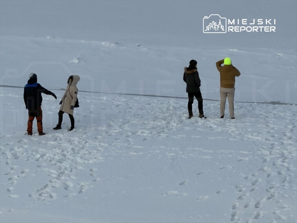 Czwórka osób na zaśnieżonym terenie, dwie rozmawiają, a dwie obserwują otoczenie.