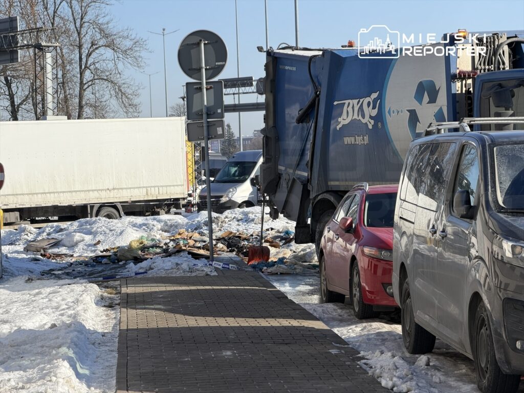 Śmieci leżą na chodniku obok zaparkowanych samochodów, a obok zatrzymany jest niebieski śmieciarka.