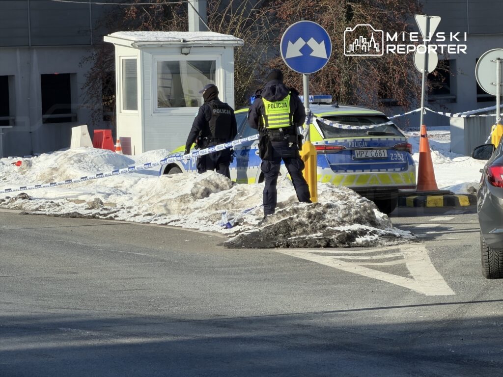 Policjanci zabezpieczają teren z niebieską taśmą, obok radiowóz na tle zasypanej śniegiem drogi.