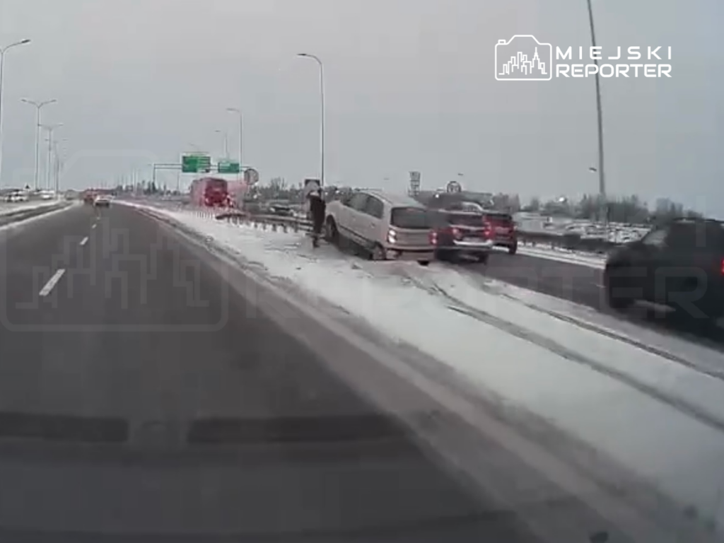 Kierowca w białym samochodzie zatrzymuje się na poboczu zaśnieżonej drogi, podczas gdy inne pojazdy przejeżdżają obok.