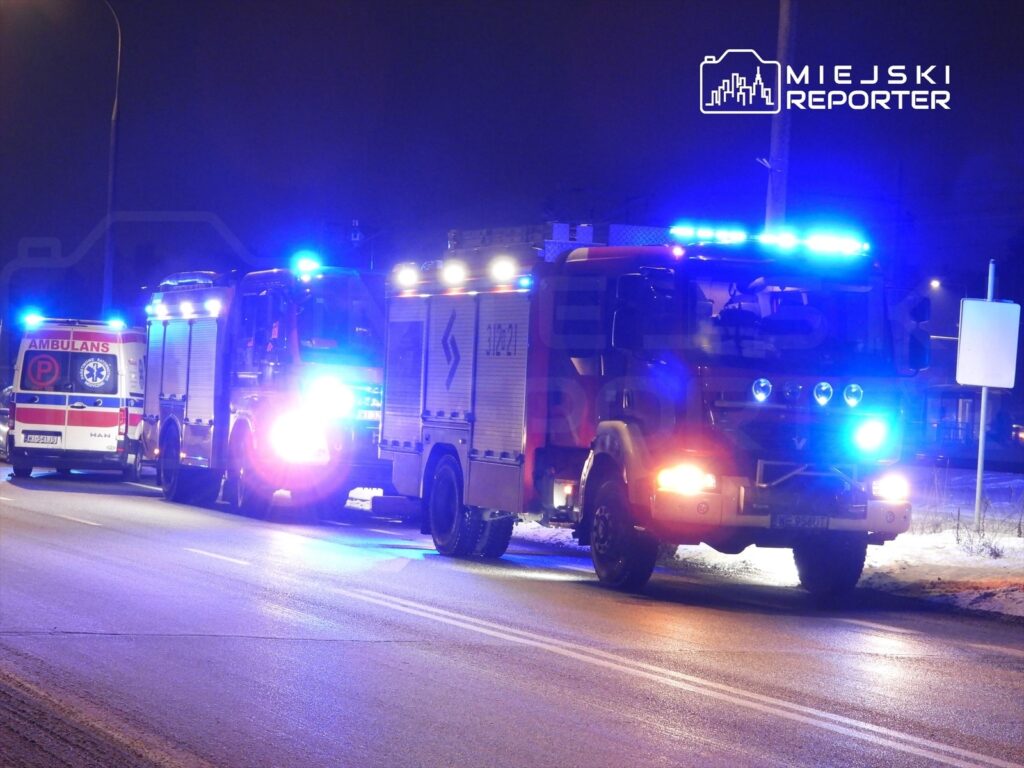 Na drodze nocą stoją dwa pojazdy ratunkowe z włączonymi sygnałami świetlnymi: ambulans i woz strażacki.