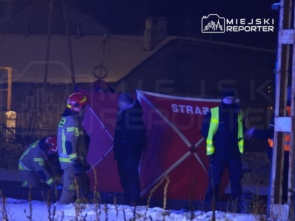 Strażacy w kaskach i mundurach pracują na terenie zdarzenia, obok czerwonego namiotu z napisem "STRAŻ".