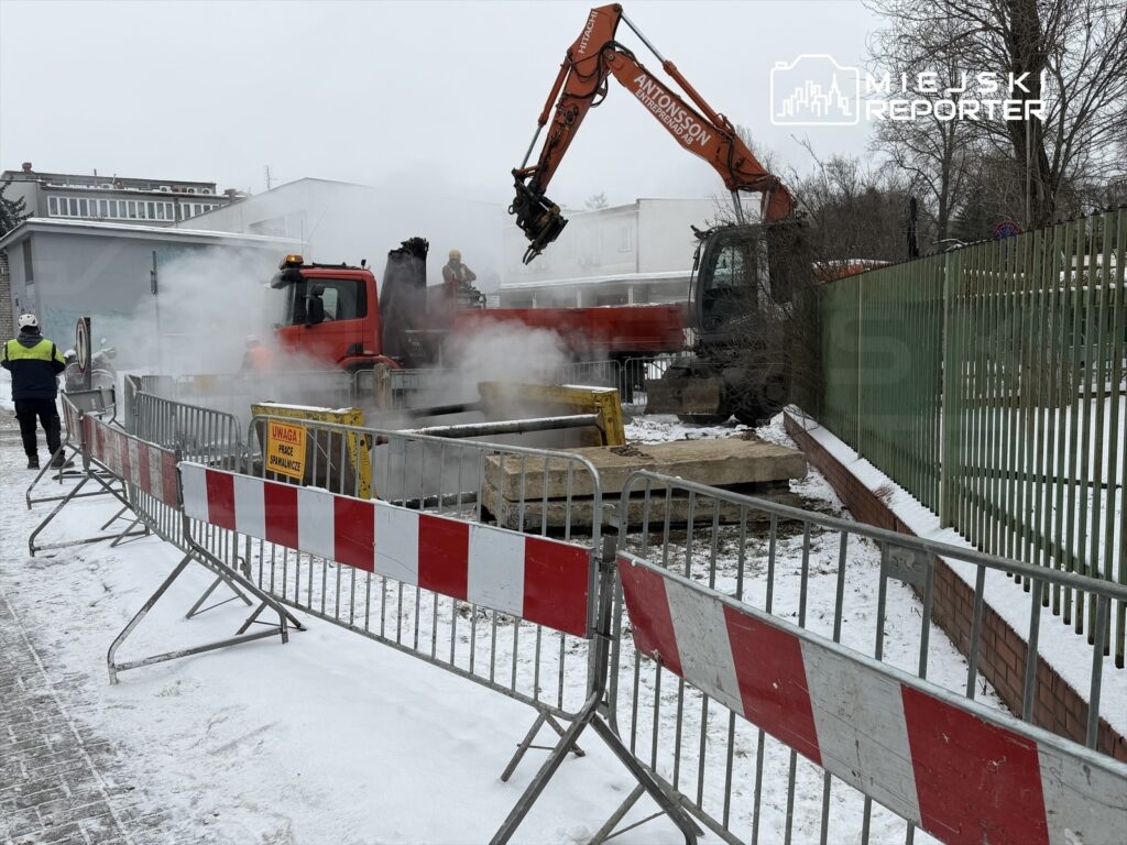 Maszyna budowlana z podnośnikiem wykonuje prace przy usuwaniu nawierzchni w zimowym otoczeniu.
