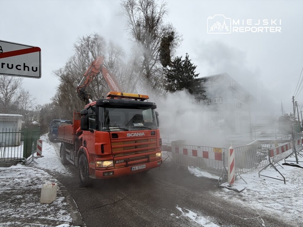 Czerwony ciężarowy samochód Scania usuwa zanieczyszczenia w zasypanym śniegiem otoczeniu, w pobliżu budynku.