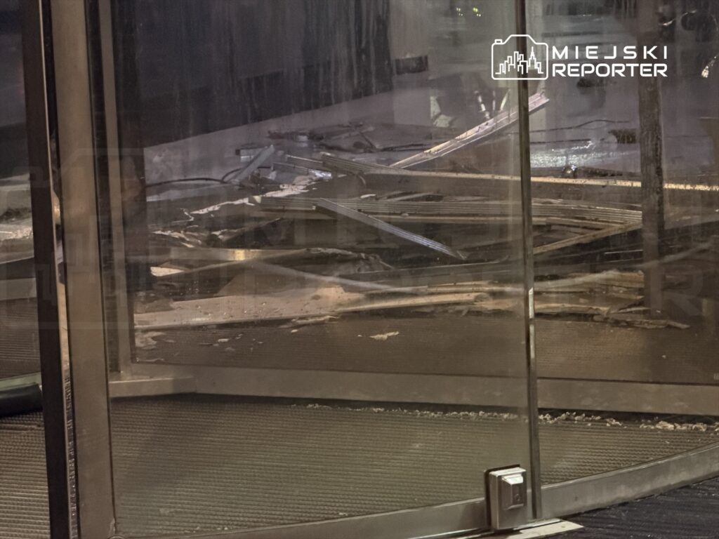 Zniszczona szklana drzwi obrotowe z fragmentami uszkodzonego mechanizmu wewnątrz budynku.