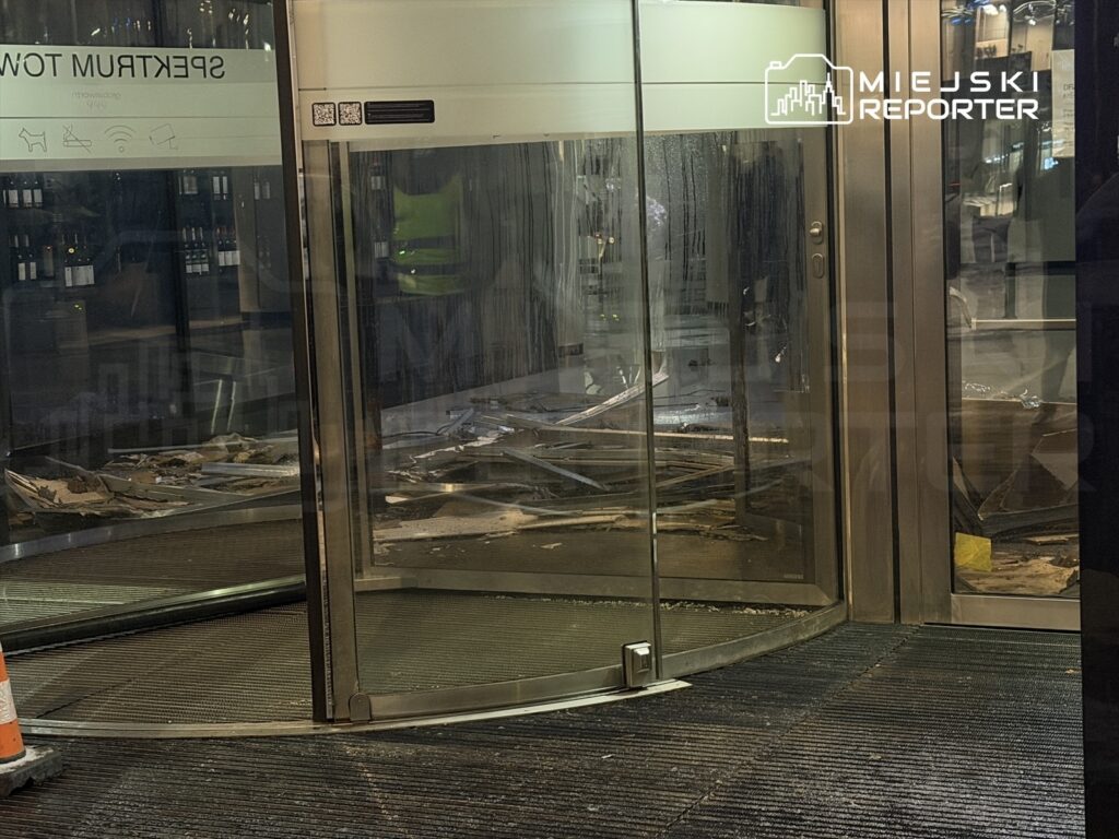 Zniszczony obrotowy drzwi z rozrzuconymi resztkami materiałów budowlanych w nowoczesnym lobby.