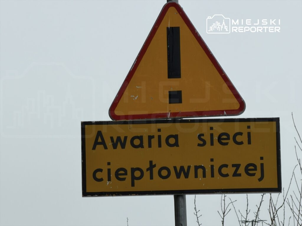 Żółty znak ostrzegawczy z napisem "Awaria sieci ciepłowniczej" umieszczony na metalowym słupie.