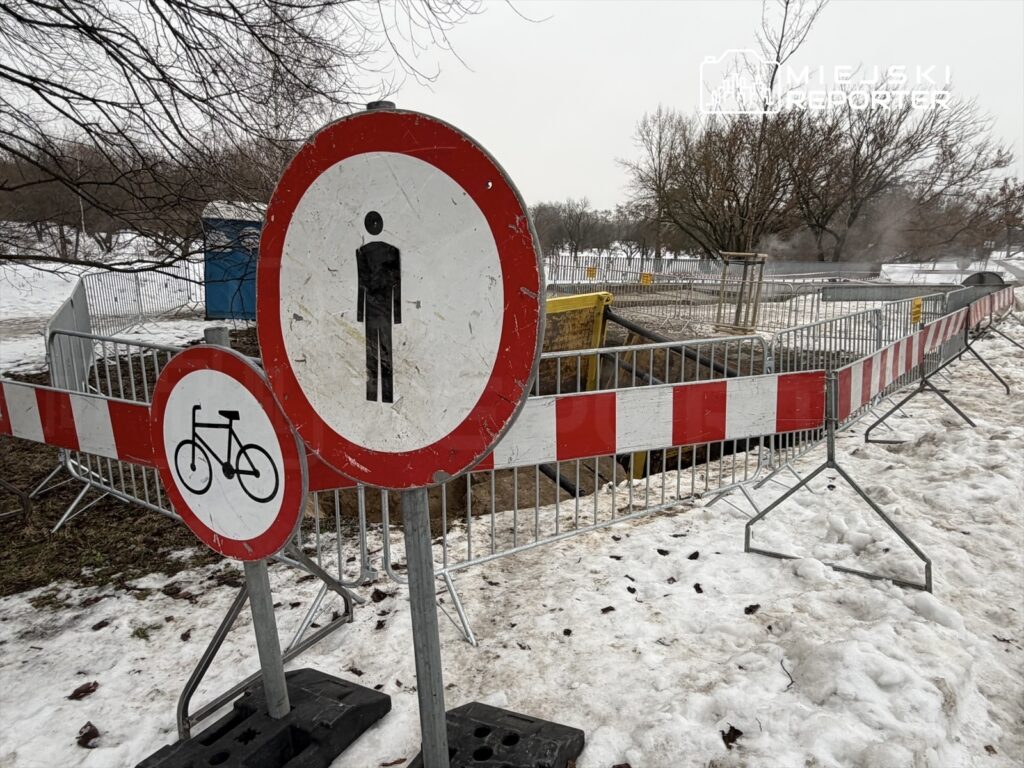 Znaki drogowe zakazujące wstępu dla pieszych i rowerzystów, otoczone barierkami w zaśnieżonym parku.