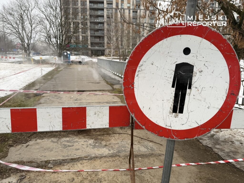 Zakaz wstępu dla mężczyzn na zamkniętej drodze, w tle widoczny nowoczesny budynek mieszkalny.