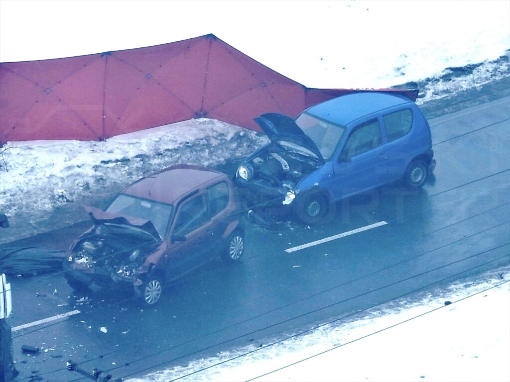 Dwa uszkodzone samochody osobowe stoją na drodze w zimowym otoczeniu, obok czerwony namiot zabezpieczający miejsce zdarzenia.