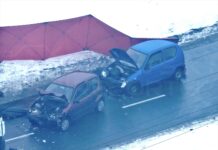 Dwa uszkodzone samochody osobowe stoją na drodze w zimowym otoczeniu, obok czerwony namiot zabezpieczający miejsce zdarzenia.