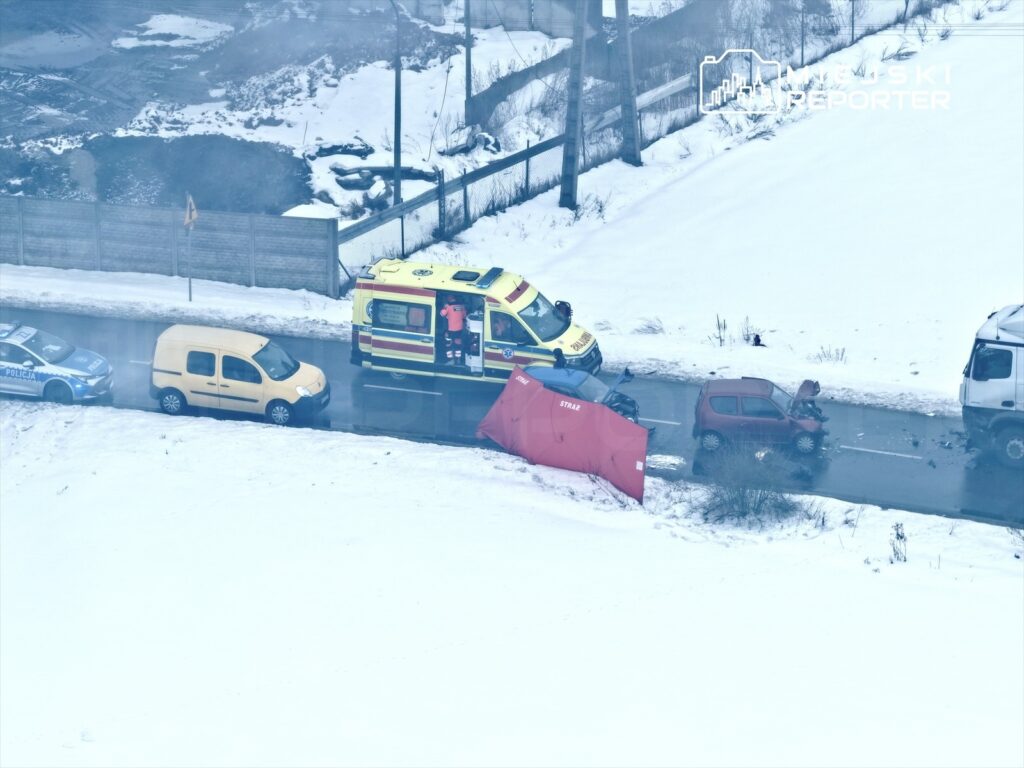 Ambulans oraz radiowóz policji zabezpieczają miejsce wypadku drogowego na zaśnieżonej drodze.