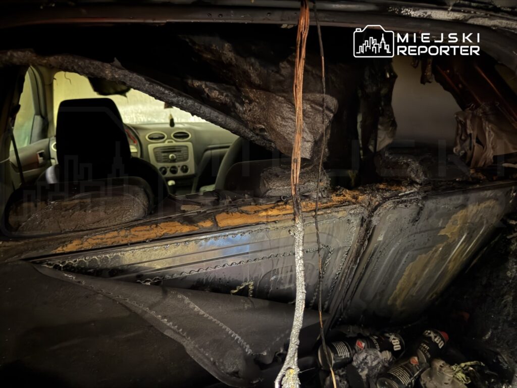 Wnętrze spalonego samochodu z uszkodzoną tapicerką i stopionymi elementami, widoczna deska rozdzielcza i siedzenia.