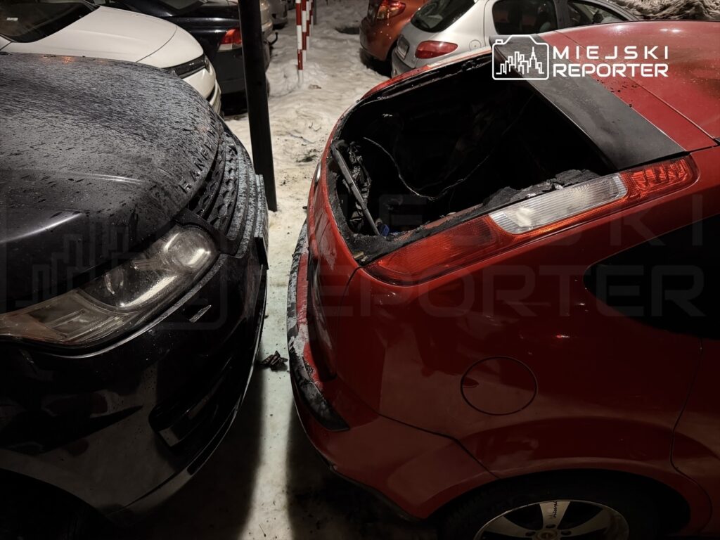 Czarne SUV zaparkowane blisko uszkodzonego czerwonego samochodu z otwartą pokrywą bagażnika na parkingu.