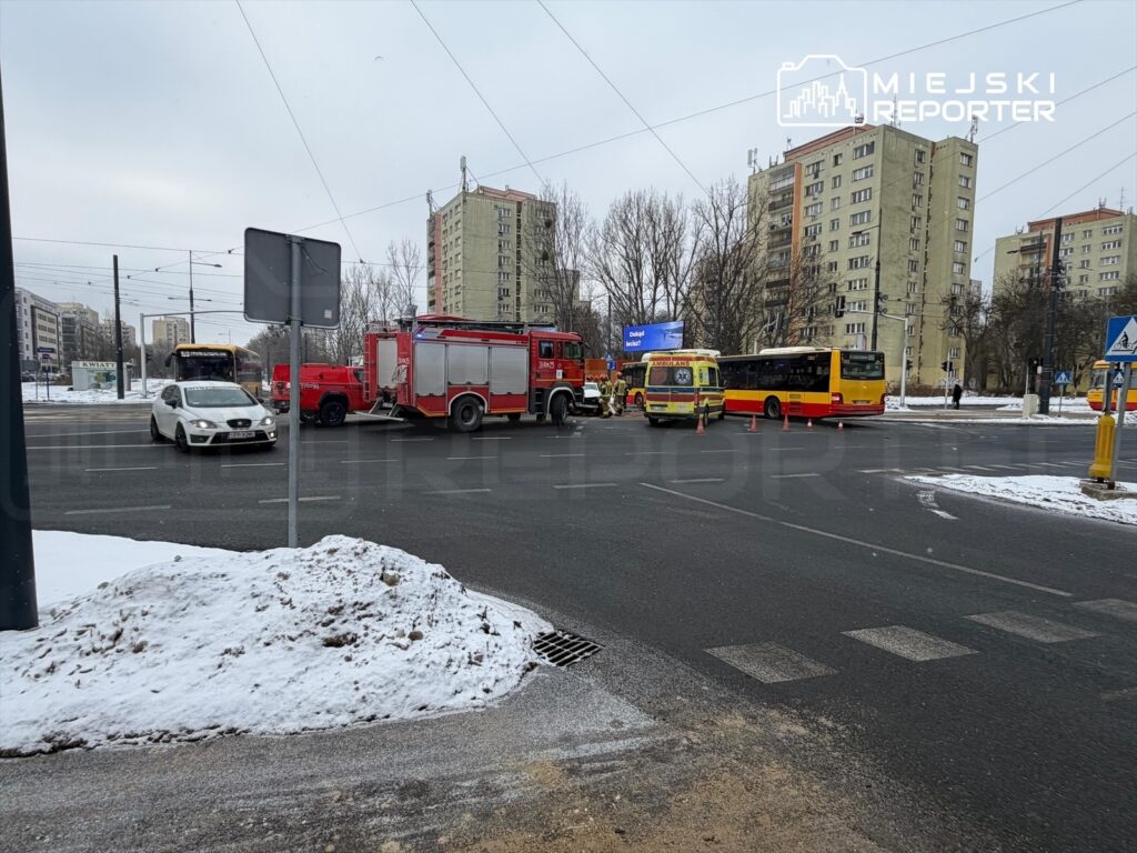 Samochody ratunkowe i straż pożarna blokują ruch na skrzyżowaniu w zimowej scenerii, obok przystanku autobusowego.