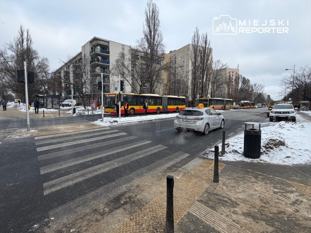 Pasażerowie czekają na przystanku autobusowym, obok przejścia dla pieszych w zimowym otoczeniu.
