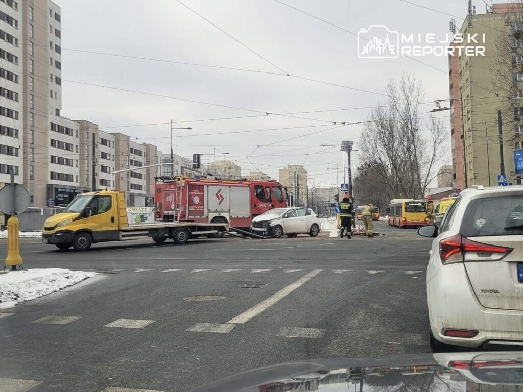 W miejscu wypadku ratownicy i strażacy pracują przy uszkodzonym samochodzie osobowym na skrzyżowaniu.