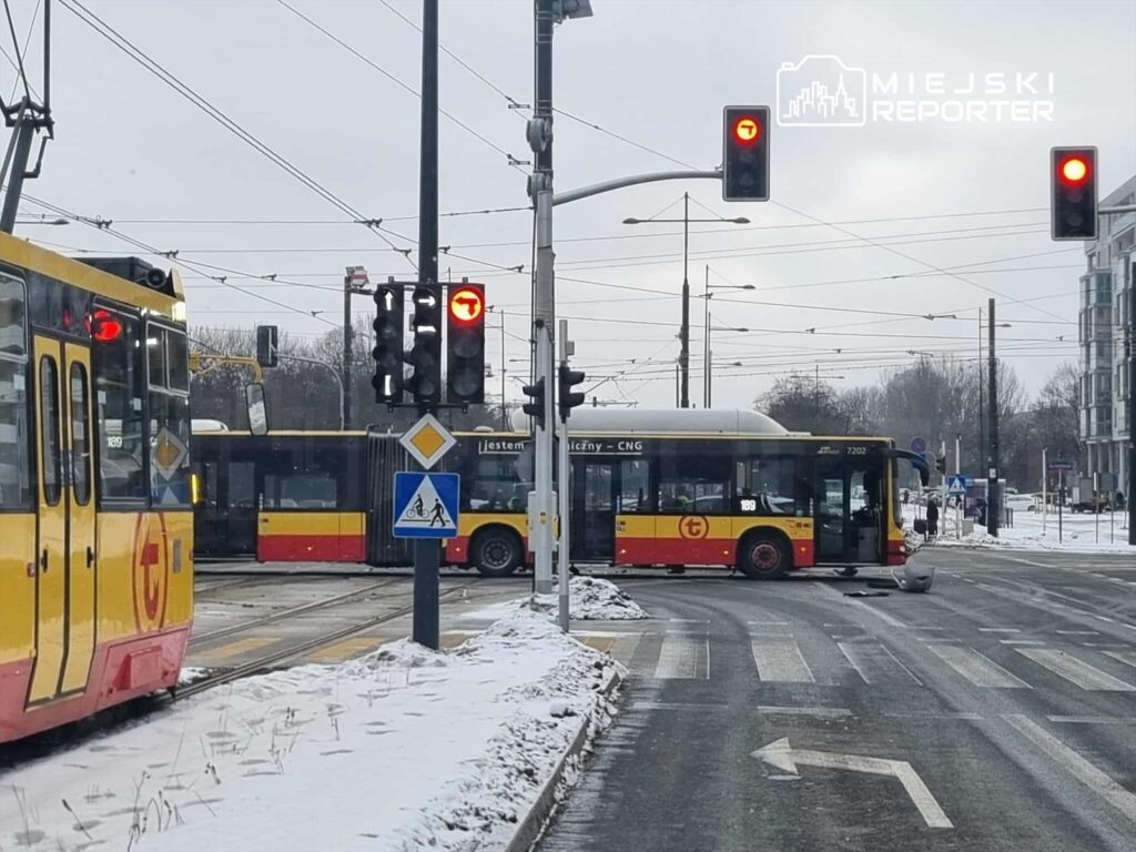 Żółty tramwaj zatrzymany na skrzyżowaniu z czerwonym sygnalizatorem, obok stoi autobus w ruchu na śnieżnej nawierzchni.