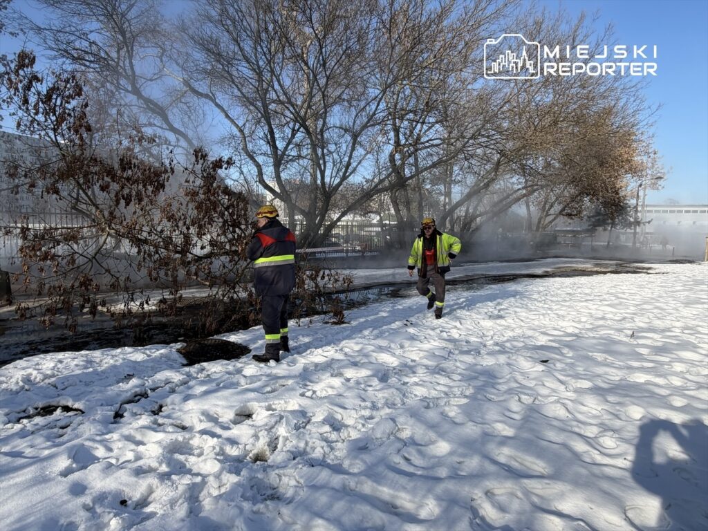 Dwóch strażaków w mundurach gaśniczych przemieszcza się w pobliżu zadymionego obszaru pokrytego śniegiem.