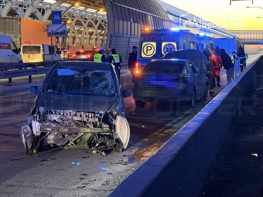 Uszkodzony samochód osobowy z otwartą maską stoi na pasie drogi, obok grupy ratowników medycznych i policjantów.