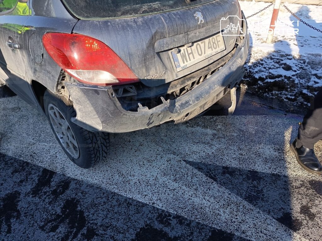 Uszkodzony samochód osobowy marki Peugeot zaparkowany na drodze, z widocznymi zniszczeniami tyłu pojazdu.