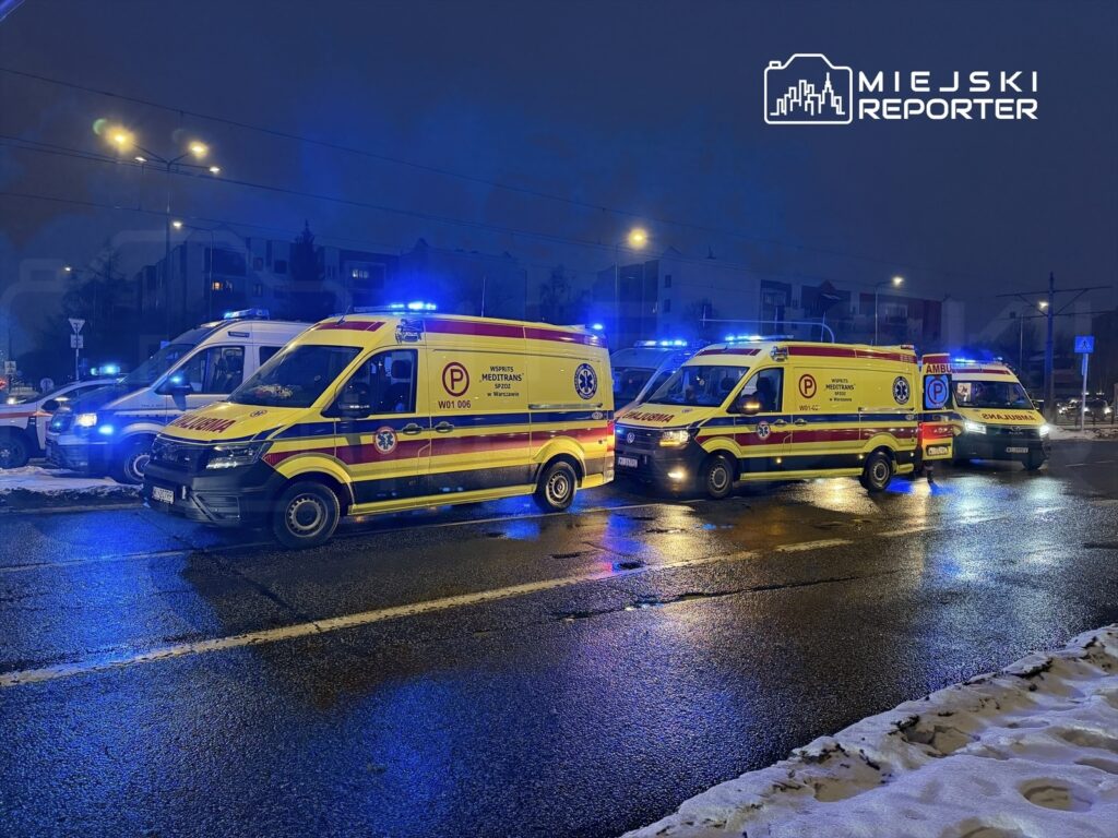 Zespół karetek pogotowia z niebieskimi sygnałami świetlnymi zatrzymany na oświetlonej ulicy w zimowej scenerii.