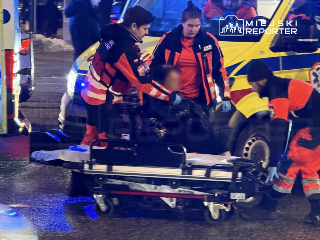 Czterech ratowników medycznych przenosi osobę na noszach w pobliżu karetki na oświetlonej ulicy.