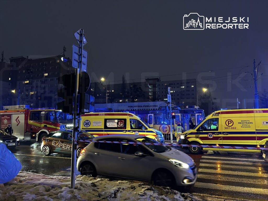Pojazdy ratunkowe blokują ruch na ulicy w nocy, w tle widać oświetlone budynki mieszkalne.