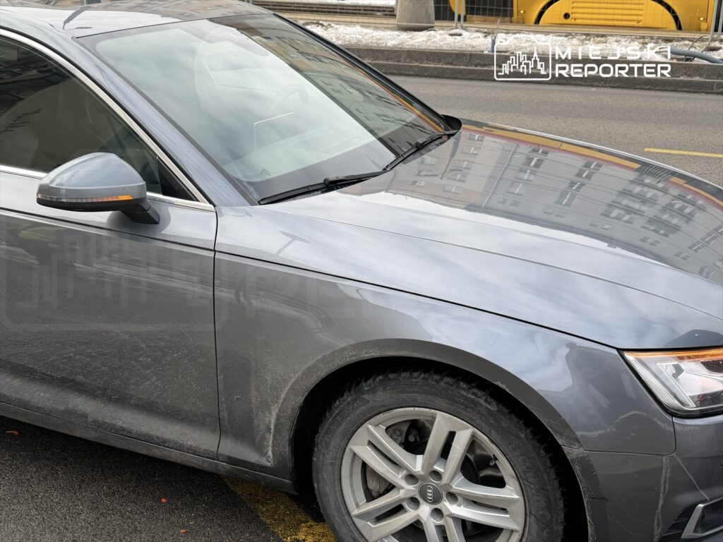 Szary samochód osobowy zaparkowany na ulicy, z widocznymi śladami brudu na karoserii.