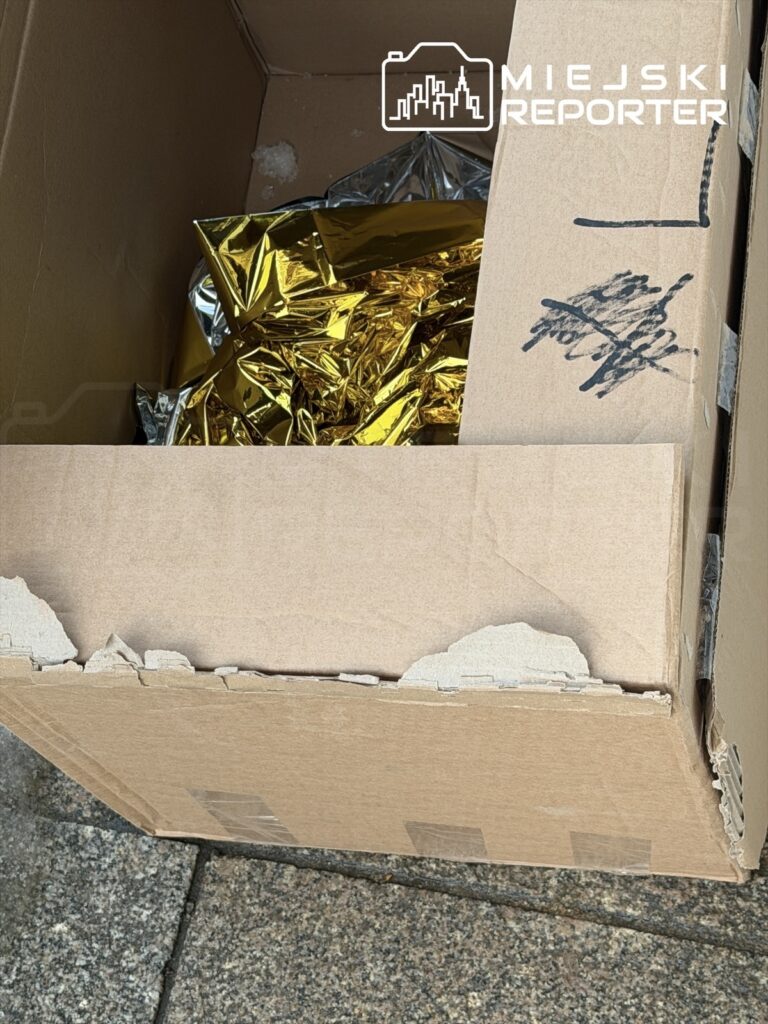 Karton z foliami w kolorze złotym i srebrnym, leżący na chodniku.