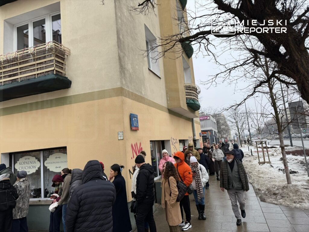 Ludzie stoją w kolejce przed sklepem z odzieżą używaną, przy zimowej, śnieżnej pogodzie.