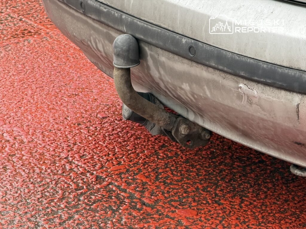 Zbliżenie na tylną część samochodu z widocznym zderzakiem i wydechem na czerwonym podłożu.