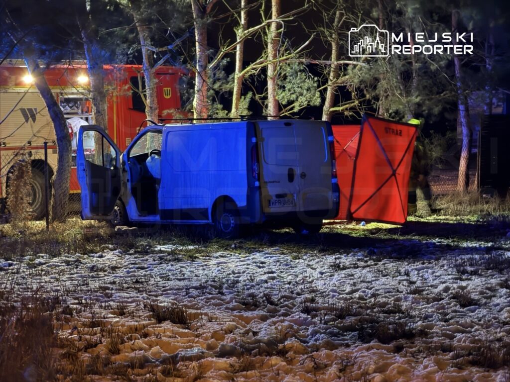 Zespół ratunkowy pracuje przy białym vanie w lesie, obok czerwonej namiotu z napisem "STRAŻ".