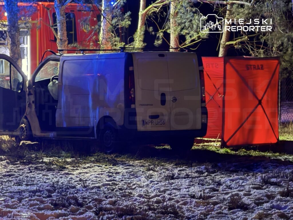 Biały furgon z otwartymi drzwiami stoi na ośnieżonym terenie, obok czerwony namiot z napisem "STRAŻ".